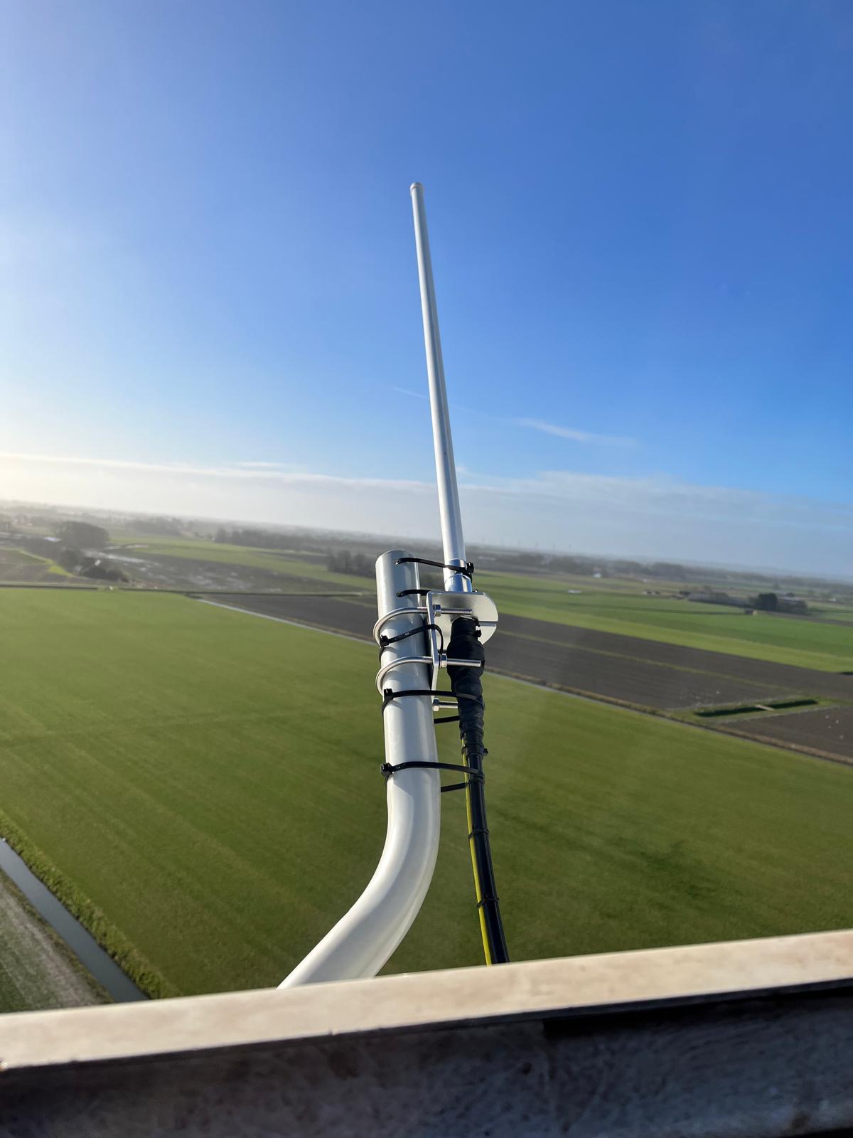 Close-up of antenna bracket on a mast over green fields