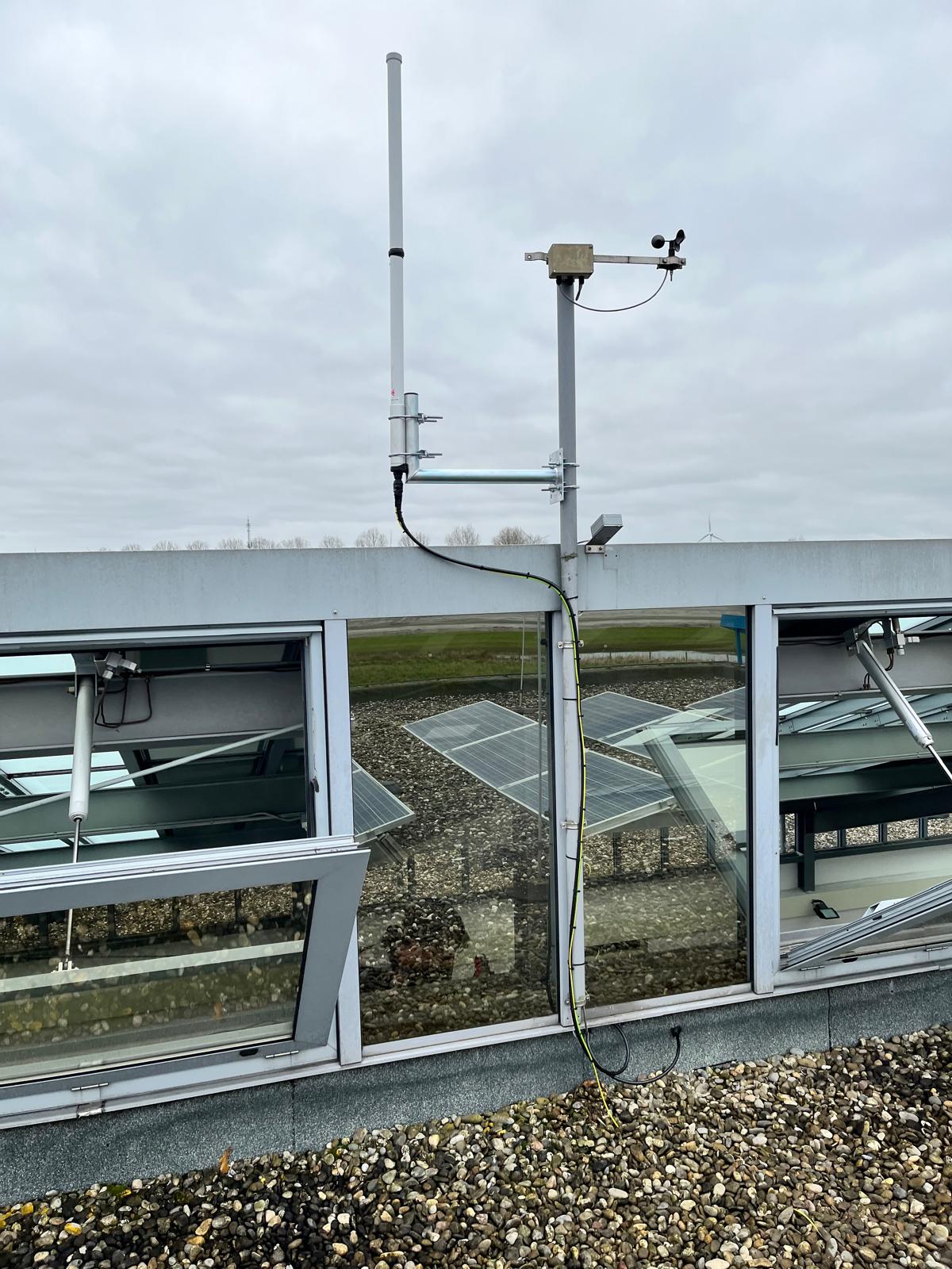 Antenna on a mast beside greenhouses with solar panels